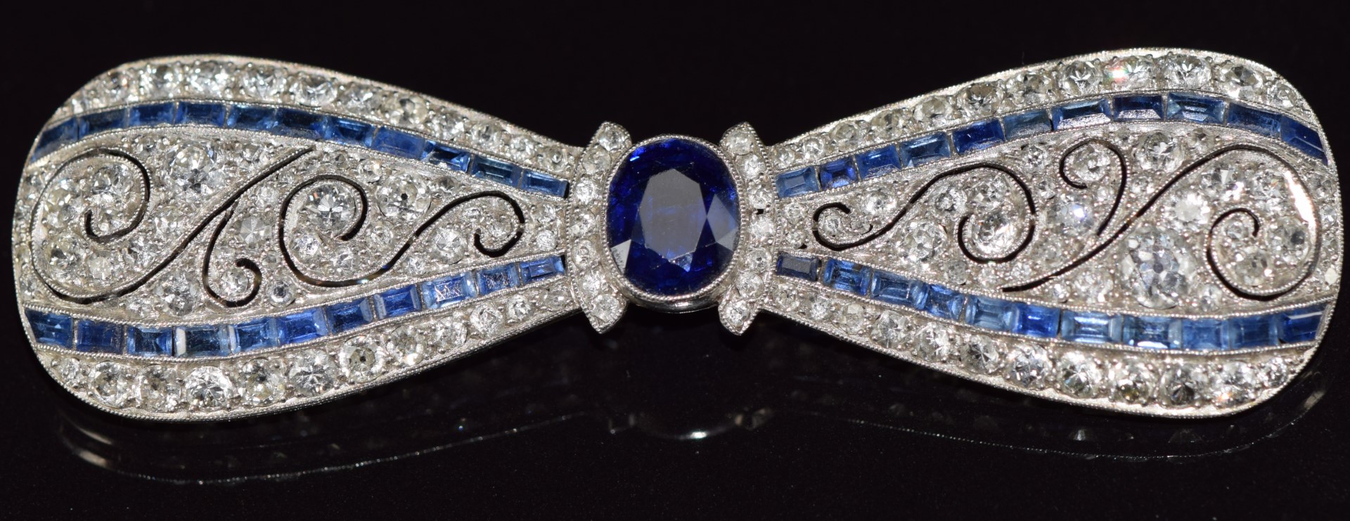 A c1915 platinum brooch in the form of a bow set with an oval cut sapphire measuring approximately