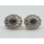(NB) A pair of Edwardian style oval ear clips, set centrally with cabochon sapphires, within an