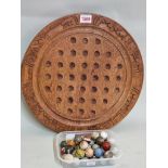 A carved teak solitaire board and thirty eight hardstone marbles, the board 38.5cm diameter.
