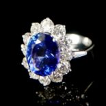 AN 18CT WHITE GOLD, OVAL AAA TANZANITE AND ROUND BRILLIANT CUT DIAMOND CLUSTER RING. (Size O).