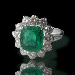 AN 18CT WHITE GOLD, EMERALD AND DIAMOND CLUSTER RING Flanked by tapered baguette shoulders. (