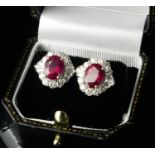 A PAIR OF 18CT WHITE GOLD, OVAL CUT TREATED RUBIES AND DIAMOND CLUSTER STUDS Complete with WGI