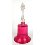 A LARGE VICTORIAN CRANBERRY GLASS HAND BELL The turned clear glass handle with cranberry bell. (