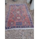 A PERSIAN WOOLLEN RUG OF CARPET PROPORTIONS Having three geometric motifs on a red ground, the