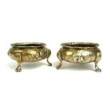 A PAIR OF VICTORIAN SILVER SALTS Having embossed floral decoration, on tripod legs terminating on