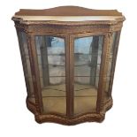 A 19TH CENTURY GILTWOOD SERPENTINE FORM DISPLAY CABINET With two glazed doors enclosing shelves,