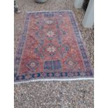 A PERSIAN DESIGN WOOLLEN RUG OF CARPET PROPORTIONS Having three geometric motifs on a red ground,