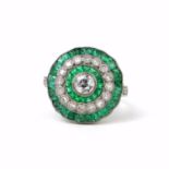 A PLATINUM EMERALD AND DIAMOND DRESS RING set with a central old-cut diamond, a halo of calibre