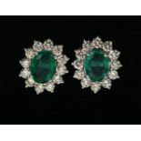 A PAIR OF 18CT WHITE GOLD OVAL EMERALD AND DIAMOND CLUSTER STUD EARRINGS. (Emeralds 3.15ct, Diamonds