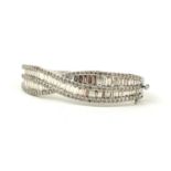 AN IMPRESSIVE LARGE 9CT WHITE GOLD TWIST STYLE DIAMOND BANGLE, SET WITH BAGUETTE CUT AND ROUND
