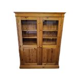 A PINE TWO DOOR BOOKCASE/CUPBOARD. (120cm x 19cm x 169cm) Condition: good throughout, some light