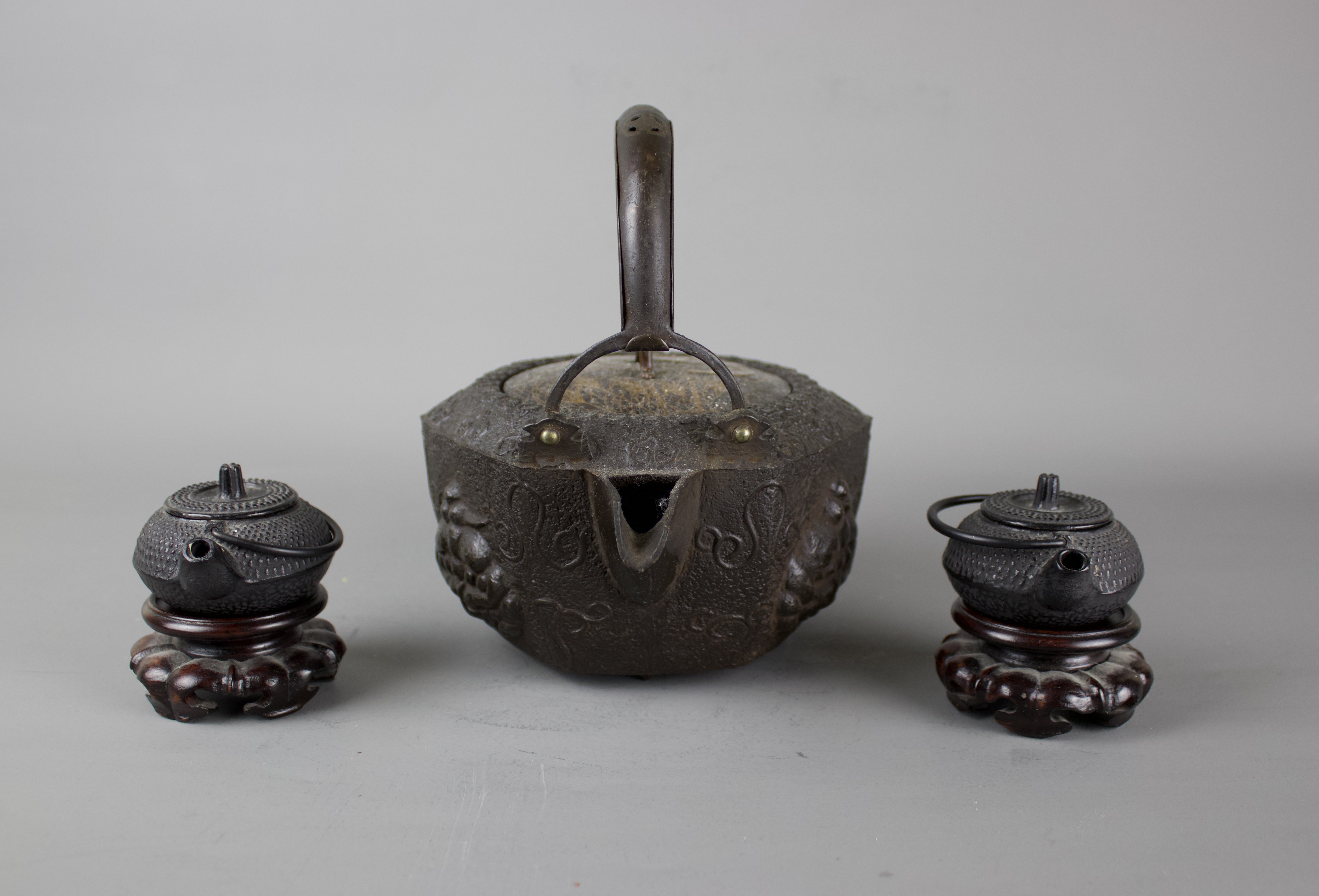 A Japanese cast iron tebsubin, 19th C and a pair of cast iron mini teapots on wooden stands, 20th C. - Image 2 of 6