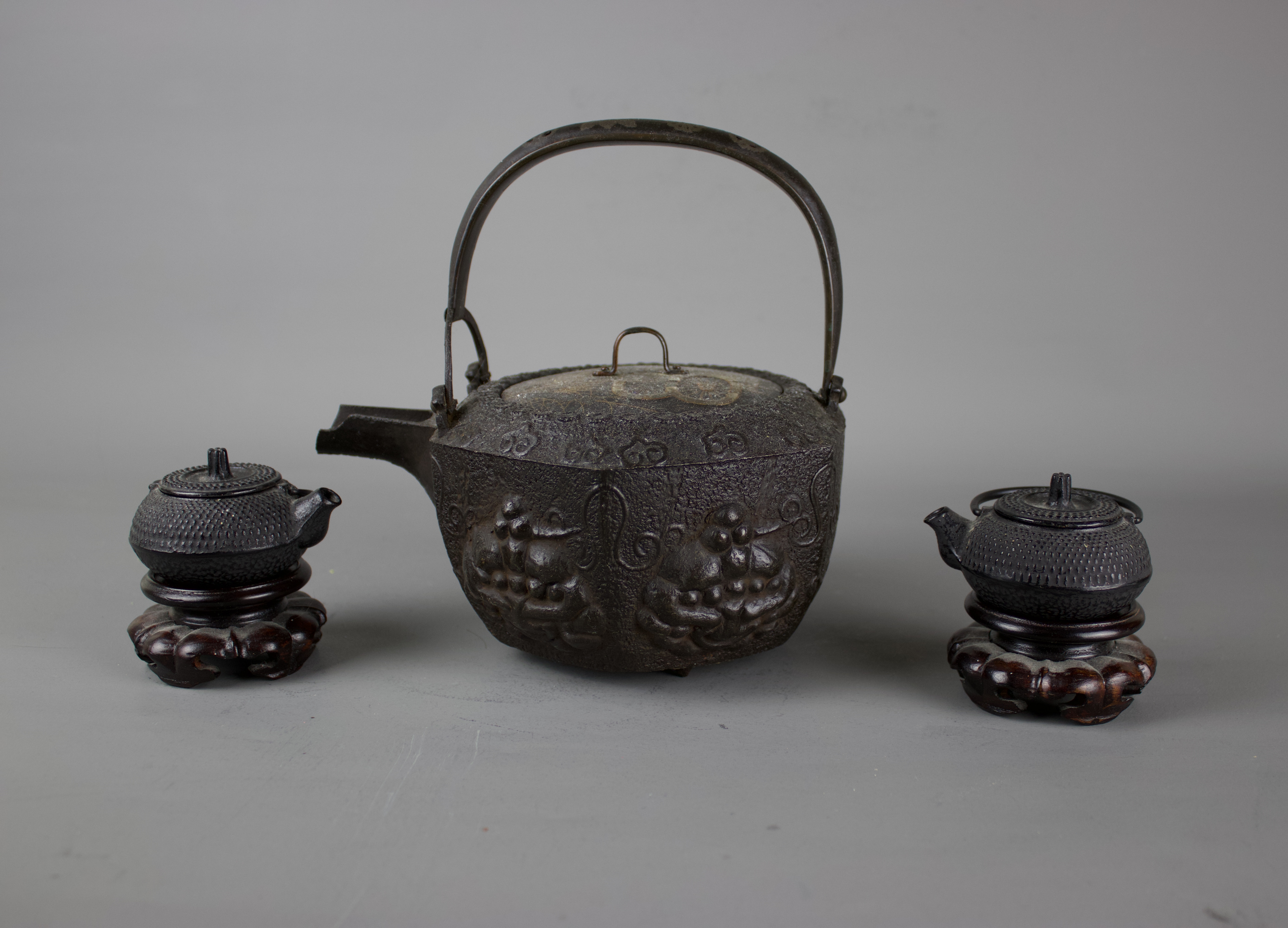 A Japanese cast iron tebsubin, 19th C and a pair of cast iron mini teapots on wooden stands, 20th C.