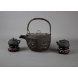 A Japanese cast iron tebsubin, 19th C and a pair of cast iron mini teapots on wooden stands, 20th C.