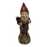 A POTTERY NOVELTY GARDEN GNOME Standing pose, with red gat, clutching a shovel, on a rustic base. (