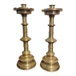 A PAIR OF CONTINENTAL ECCLESIASTICAL BRASS CANDLESTICKS With pierced drip trays, ring turned columns