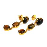 A PAIR OF YELLOW METAL AND TIGER'S EYE DROP EARRINGS Set with three graduated oval cut stones on