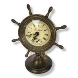 A BRONZE SHIPS WHEEL MECHANICAL CLOCK ON STAND With Roman numeral clock face and a smaller minute