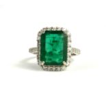 AN 18CT WHITE GOLD LARGE EMERALD CUT EMERALD AND ROUND BRILLIANT CUT DIAMOND CLUSTER RING with