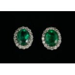 A PAIR OF 18CT WHITE GOLD OVAL EMERALD AND DIAMOND CLUSTER STUDS, Boxed. (Emeralds 3.96ct,