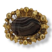 A 19TH CENTURY YELLOW METAL AND AGATE BROOCH Central oval cut stone in a wide scrolled and pierced