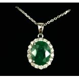 AN 18CT WHITE GOLD OVAL EMERALD AND DIAMOND CLUSTER PENDANT on an 18" silver anchor chain. (Boxed