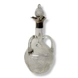 AN EDWARDIAN SILVER AND CUT GLASS DECANTER Having a silver collar, three handles and cut facets to