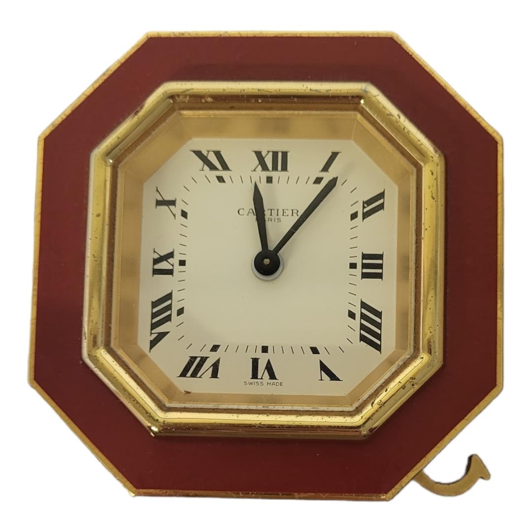 CARTIER, MUST DE CARTIER, A VINTAGE GILT METAL AND ENAMEL TRAVEL CLOCK Octagonal form with red