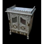 A 20TH CENTURY THAI WHITE METAL CLAD AND RELIEF DECORATED PRAYER CABINET With two mesh doors above