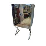 A STAINLESS STEEL DRINK'S CABINET ON STAND With two doors enclosing shelves, on cross leg