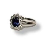 WHITE METAL, SAPPHIRE AND DIAMOND CLUSTER RING The single oval cut sapphire edged with round cut
