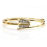 A two coloured gold diamond set hinged bangle,