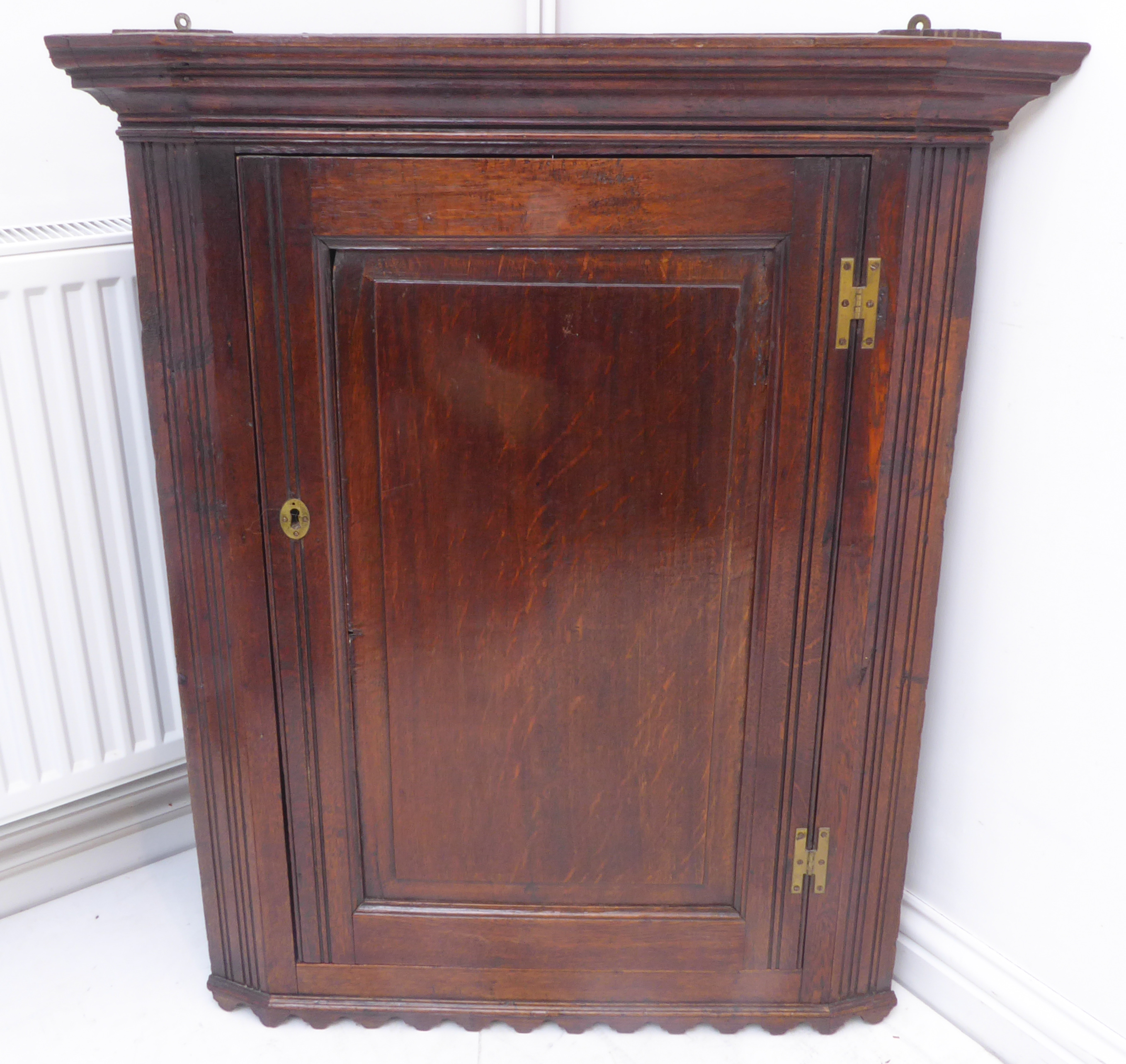 A late 18th century oak hanging corner cupboard; the single fielded panel door with brass H-form