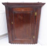 A late 18th century oak hanging corner cupboard; the single fielded panel door with brass H-form