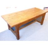 A large farmhouse-style pine table with central side drawer; the overhanging top above square legs