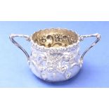 An early 20th century two-handled white-metal sugar –  decorated in repoussé style with leaves,