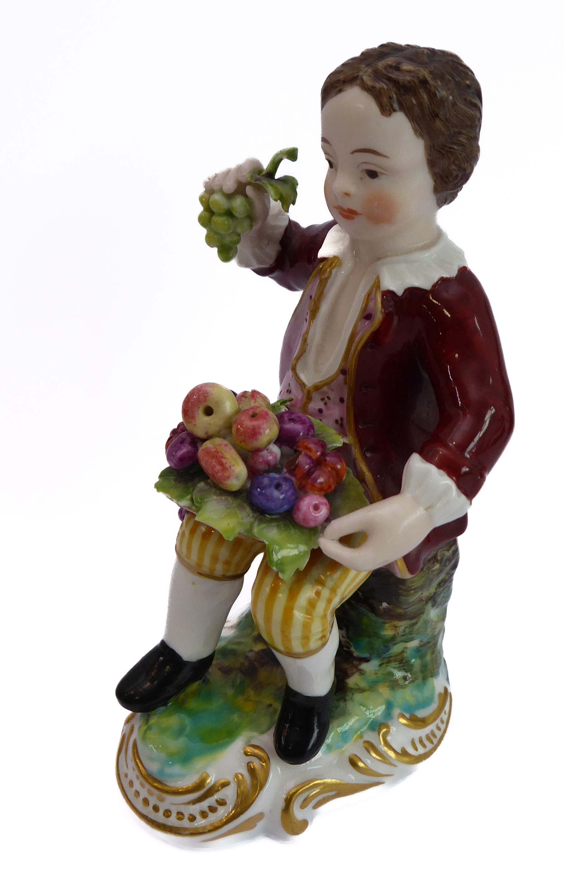 A hand-decorated Derby-style porcelain figure of a young boy - seated and holding in his right