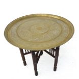 An early 20th century circular brass topped Benares style table on folding base with bobbin-turned
