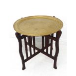 An early 20th century circular brass-topped table with folding oak base in Arts and Crafts style (