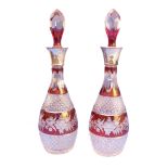 A pair of red flash-cut mallet-shaped decanters with faceted spire stoppers; the necks with