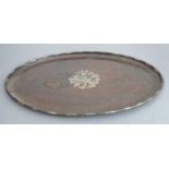 A late 19th/early 20th century hand-planished oval copper tray centrally inlaid with silver coloured