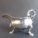 A hallmarked silver sauceboat of small proportions, leaf-capped scrolling handles and on three