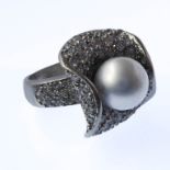 An unusual silver dress ring, central pearl surrounded by small hand-cut white stones within '