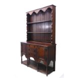 An early 20th century oak dresser; the superstructure with wavy cornice above shelves and the