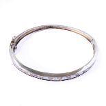 A silver bangle with hinged opening set with a multitude of baguette style white stones (total