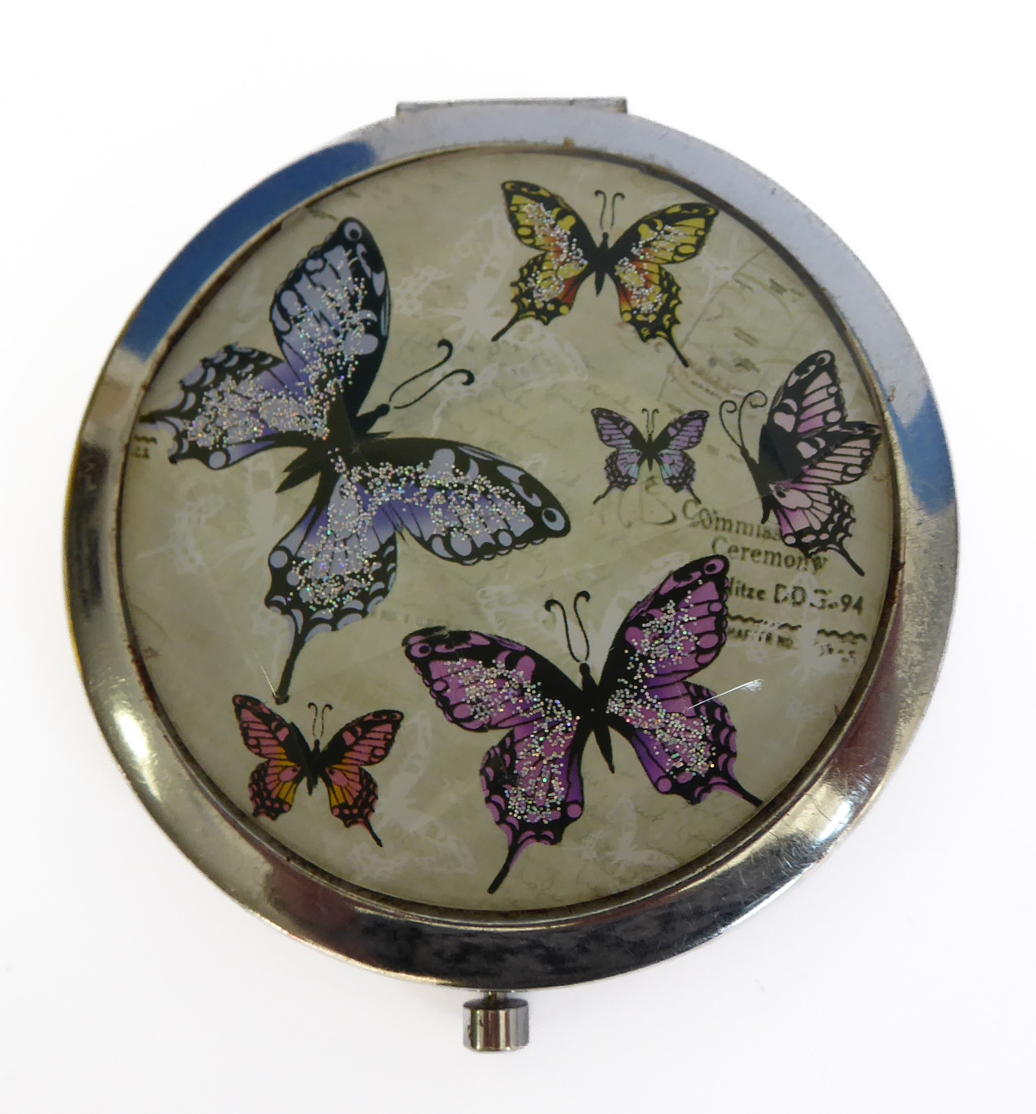 A mid-20th century circular powder compact, faceted glass lid decorated with glitter butterflies (