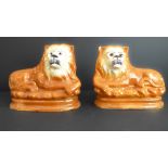 A pair of 19th century Staffordshire pottery lion figures in recumbent pose and with moulded oval