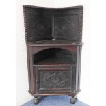 A freestanding antique oak corner cupboard: the gallery with two carved lozenges with central