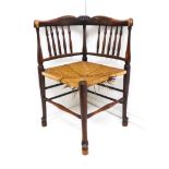 An early 20th century corner-chair with spindle back, rush seat and turned legs