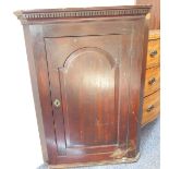 An 18th century hanging oak corner cupboard: dentil cornice above a fielded panel door opening to